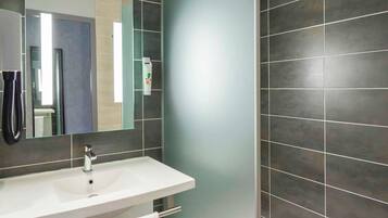 Une salle de bain moderne avec un lavabo blanc, un miroir et des murs recouverts de carreaux foncés.