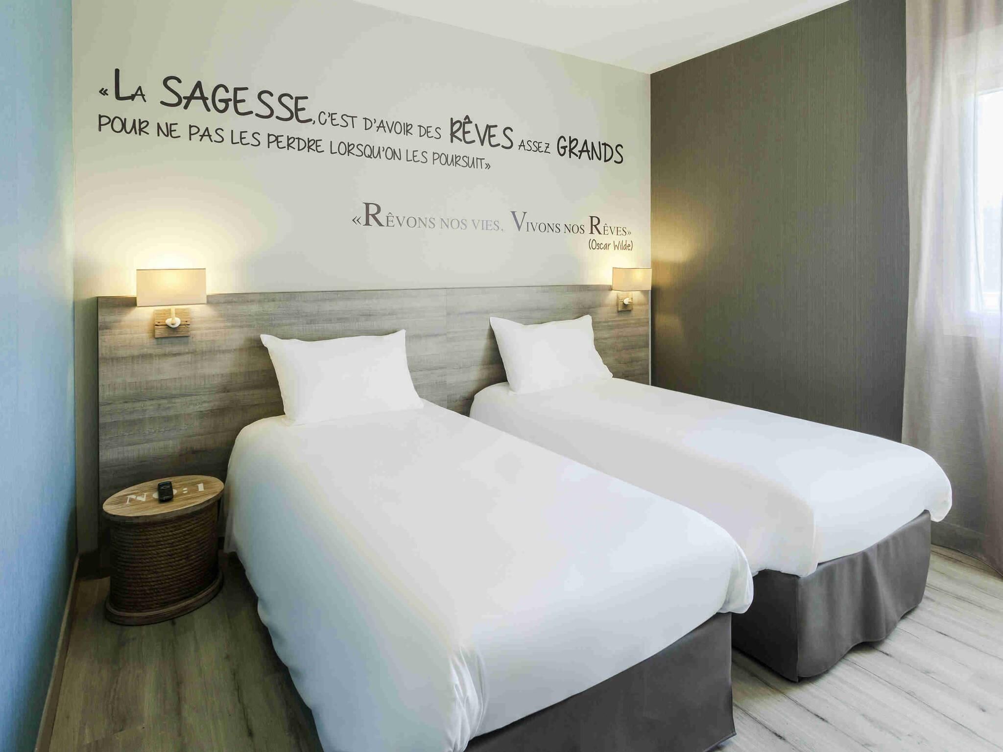 A hotel room with two beds, a wall quote, and bedside lamps.