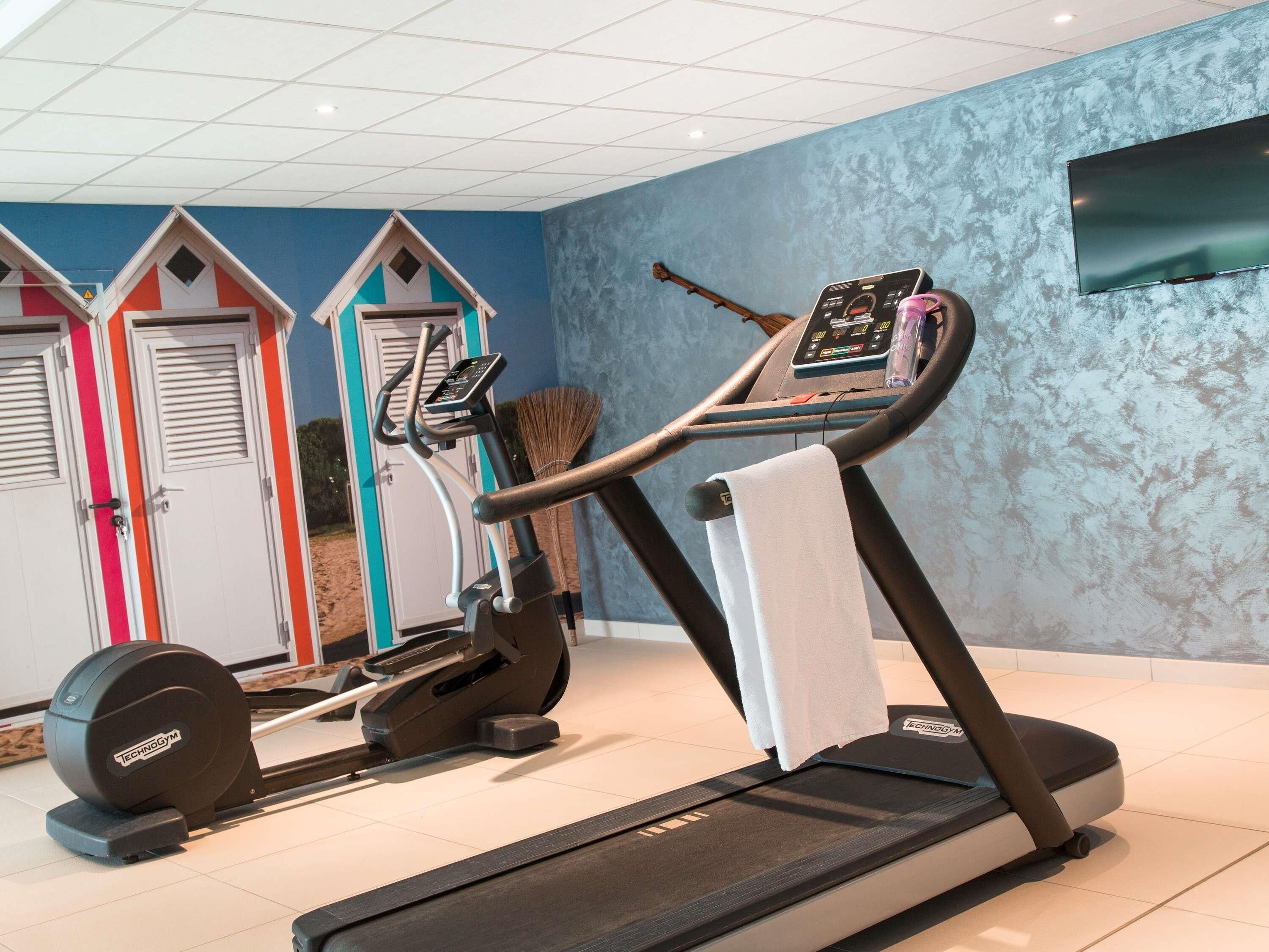 Un gimnasio con cinta de correr, pesas y una televisión instalada en la pared.