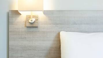A bed with white bedding, a wooden headboard, and a wall-mounted light fixture.