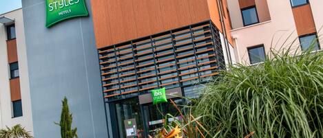 A modern hotel building with a prominent green 'ibis Styles Hotels' sign.