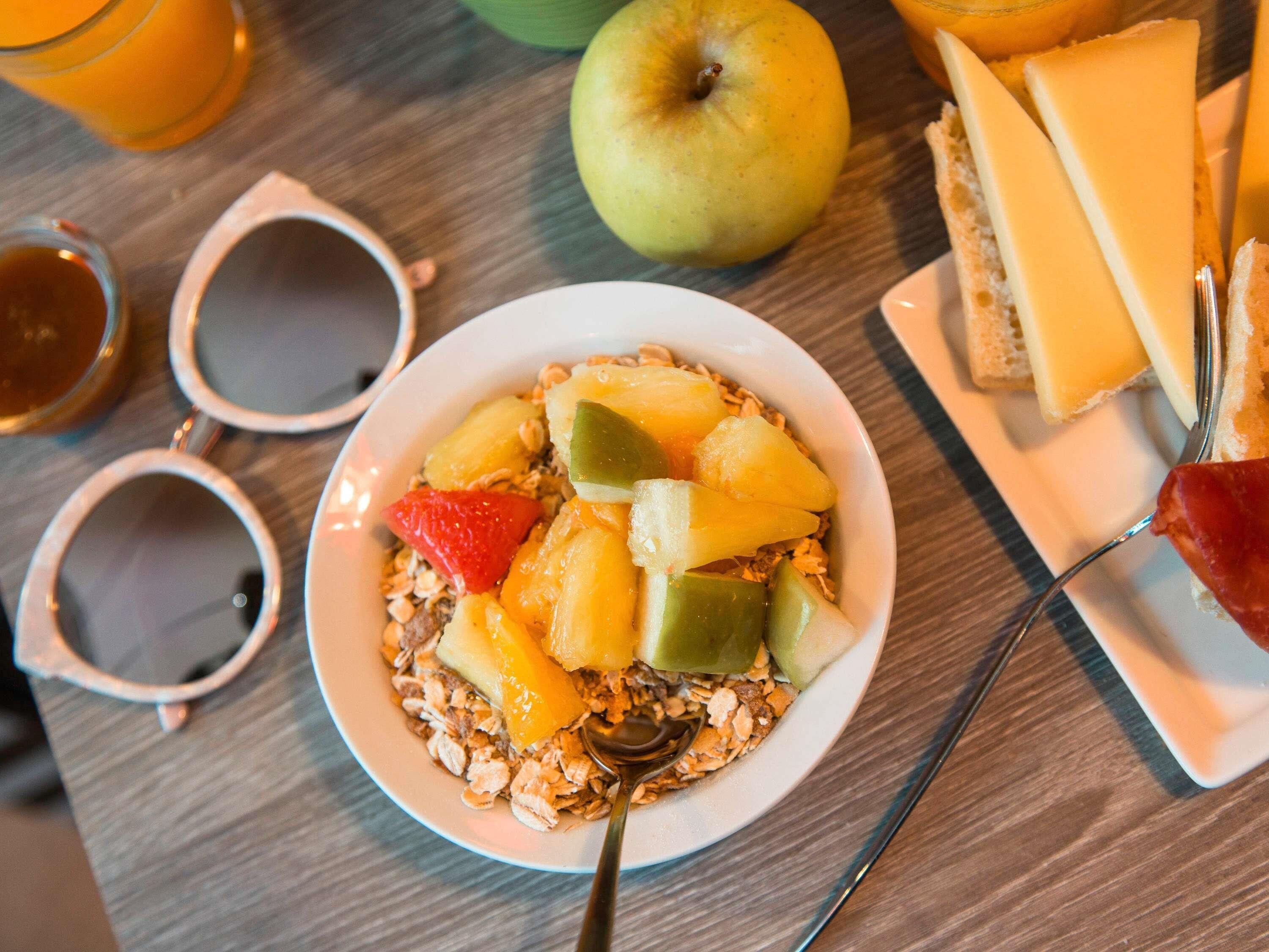 Une table mise pour le petit-déjeuner, avec un bol de céréales, des fruits et du fromage.