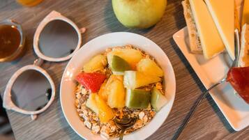Une table mise pour le petit-déjeuner, avec un bol de céréales, des fruits et du fromage.