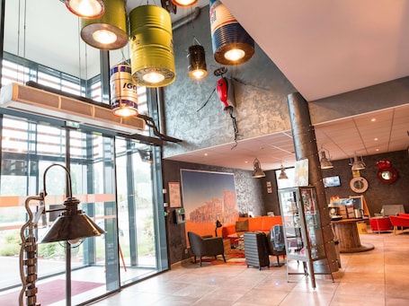 A modern hotel lobby with large windows, a reception desk, and a seating area.. Ibis Styles Vierzon