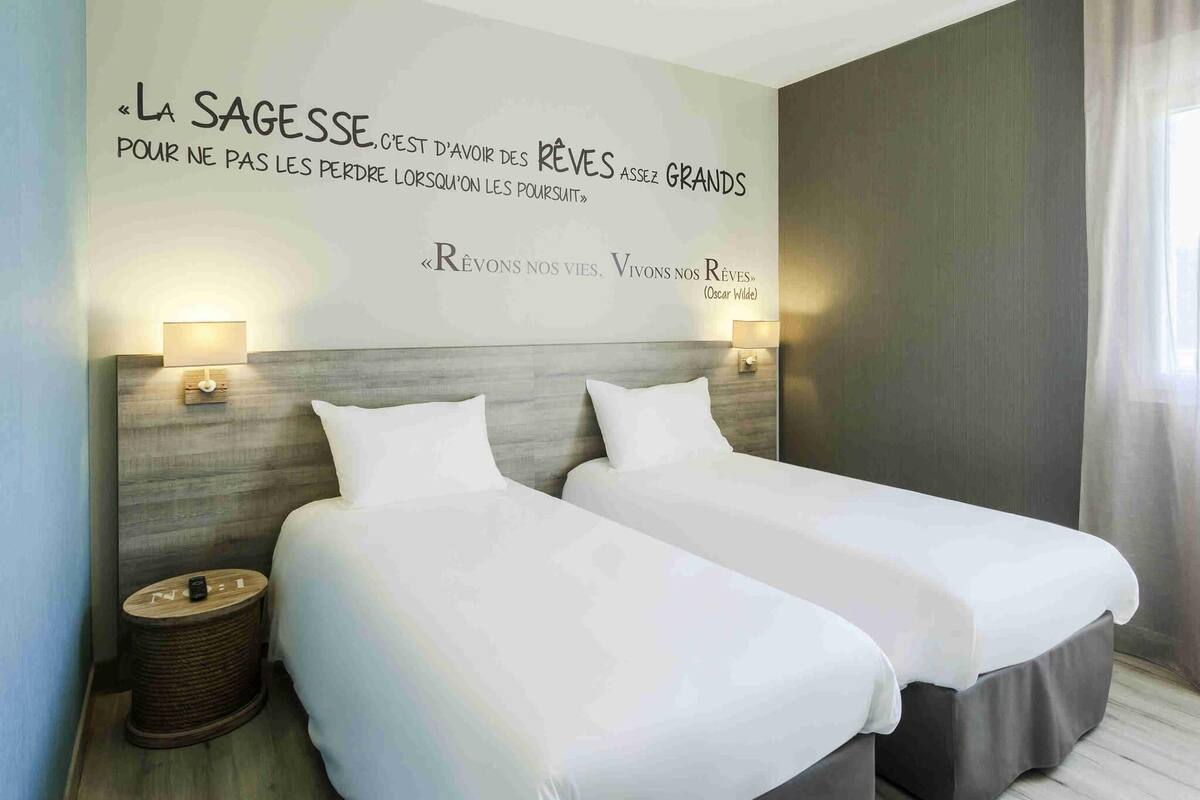 A hotel room with two beds, a wall quote, and bedside lamps.