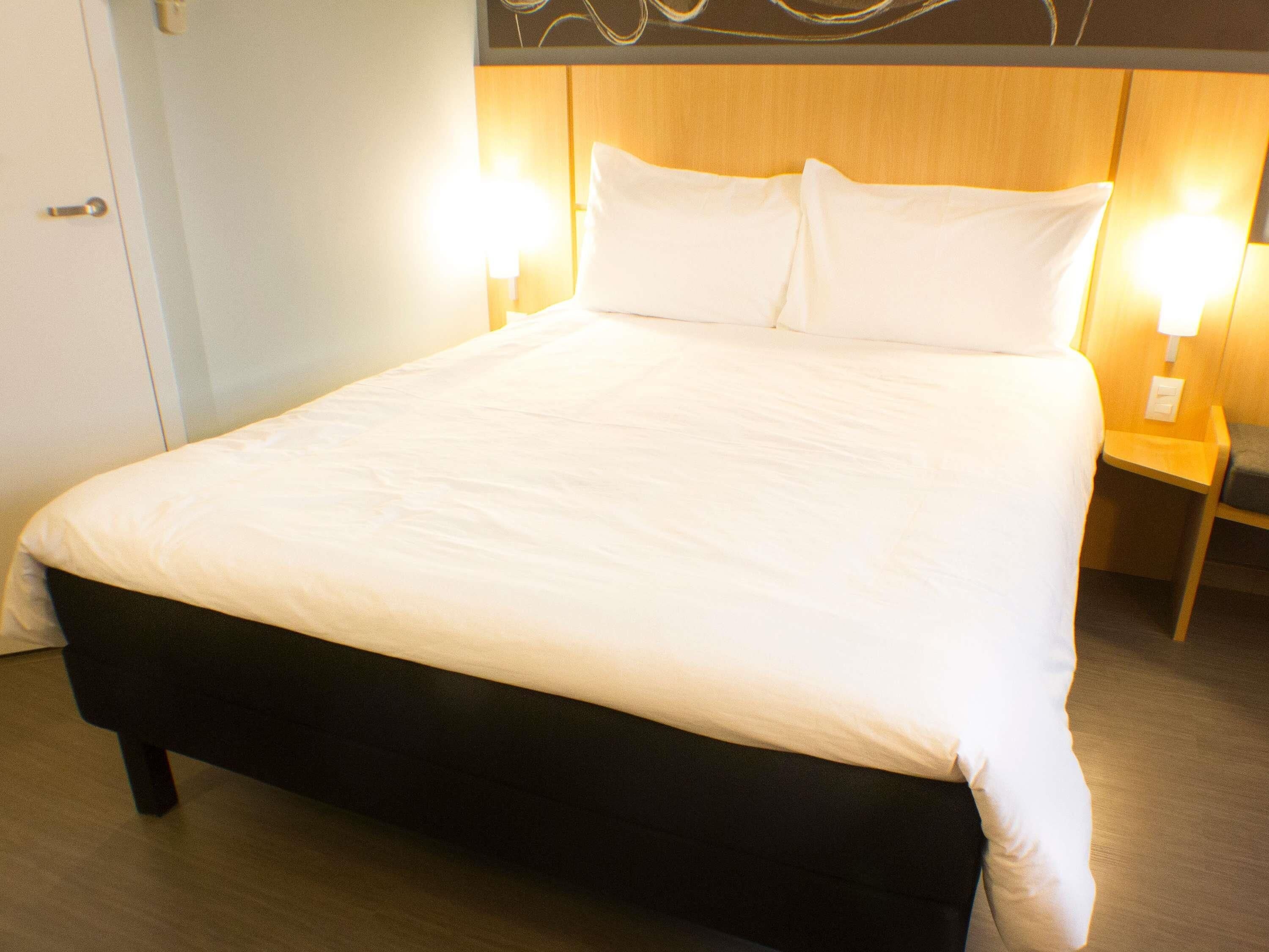 A neatly made bed with white linens, two bedside lamps, and a wooden headboard.