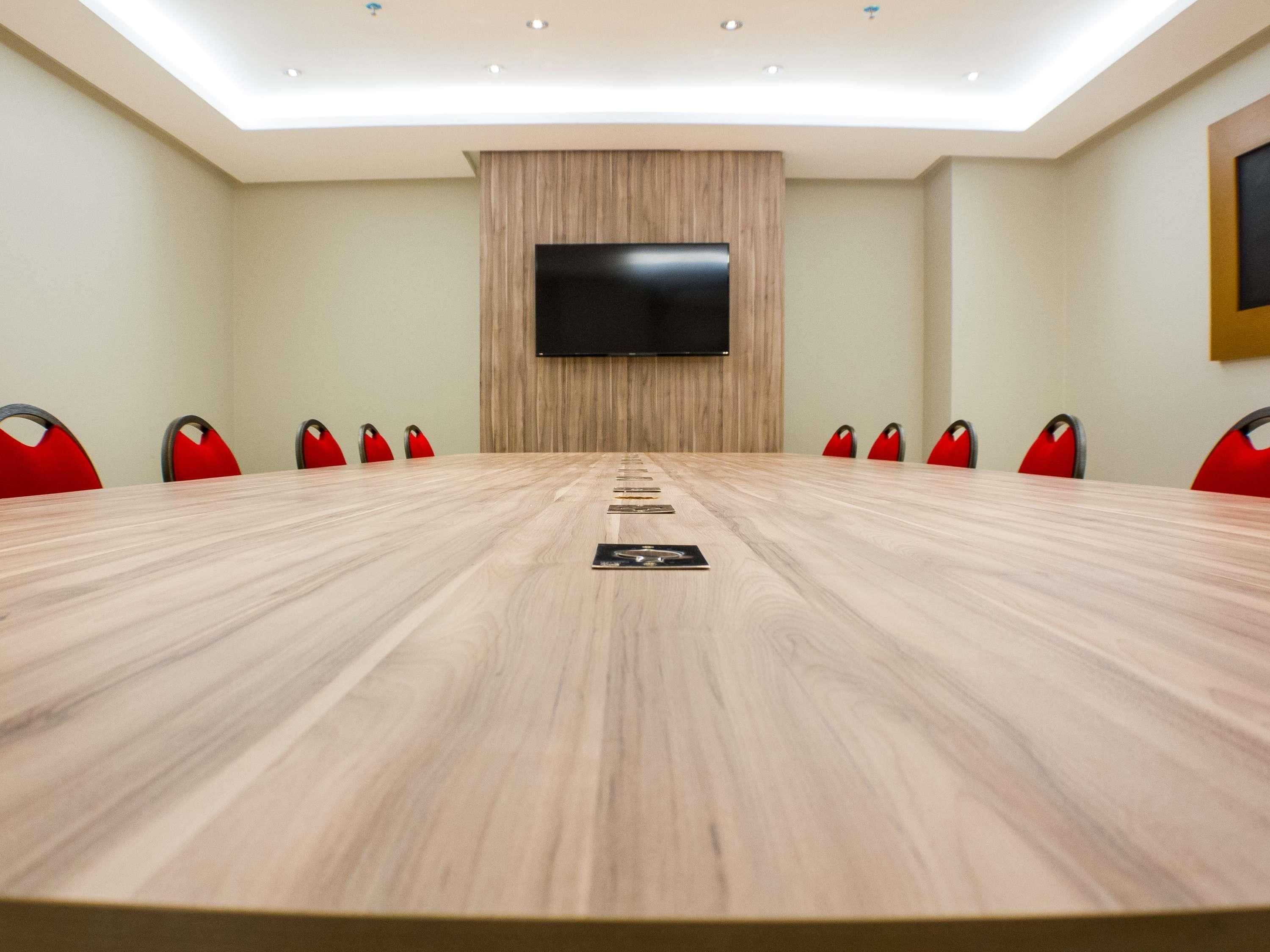 A conference room with a long table, red chairs, a flat-screen TV, and a wooden accent wall.
