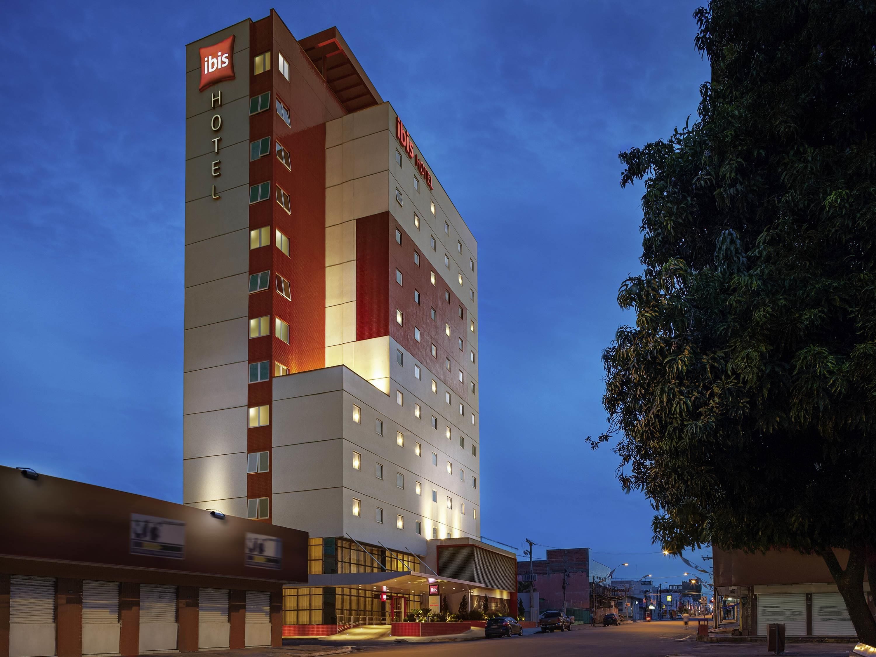 Un hotel de varios pisos con un llamativo letrero de 'ibis Hotel', que presenta un diseño arquitectónico moderno con una combinación de colores rojo y blanco.