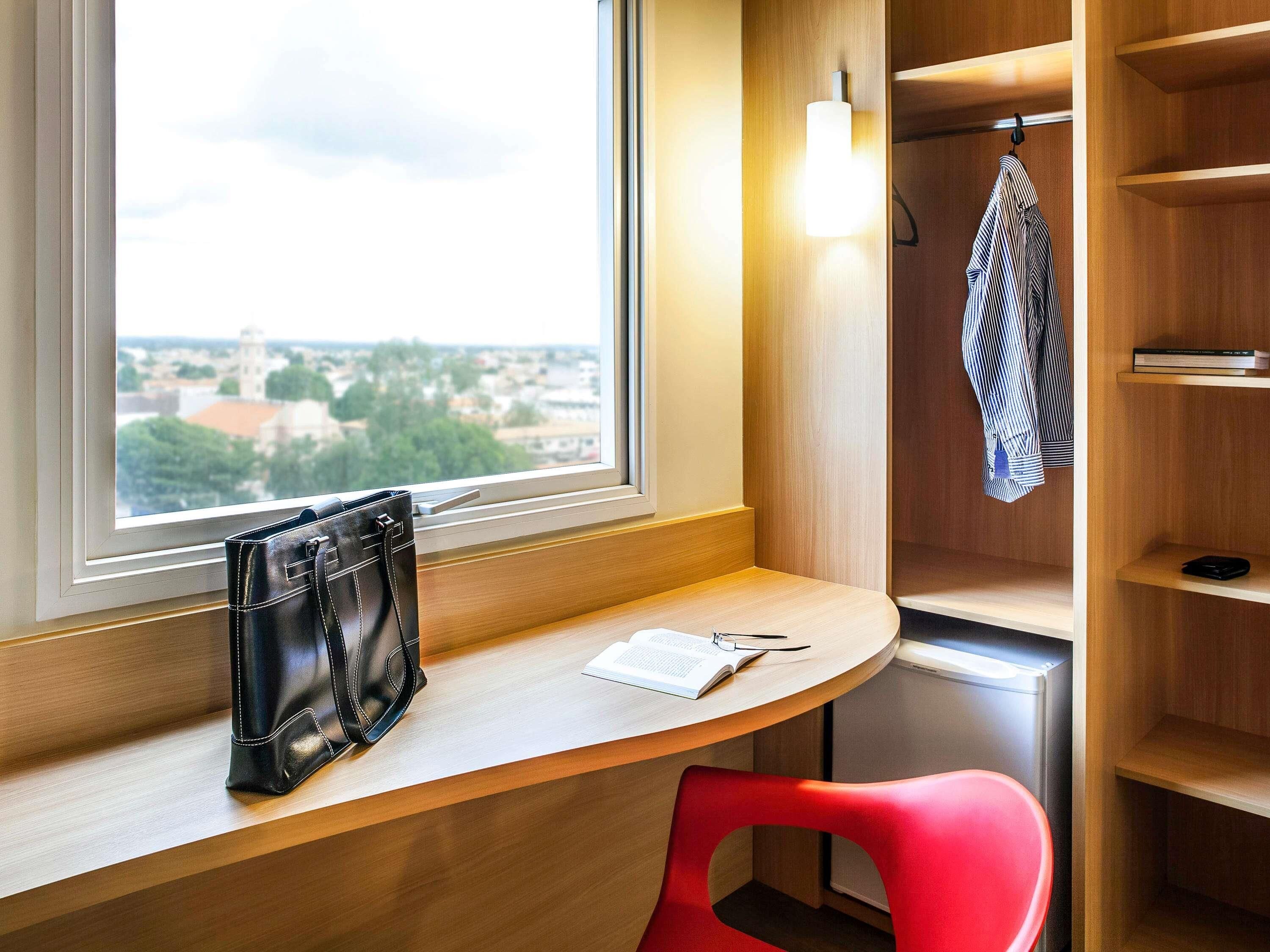 Una habitación con un escritorio, una silla roja, un bolso negro, una libreta y un bolígrafo.