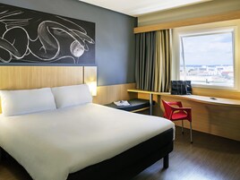 Habitación de hotel con una cama grande, un escritorio con silla, ventana con cortinas y vista a la ciudad.