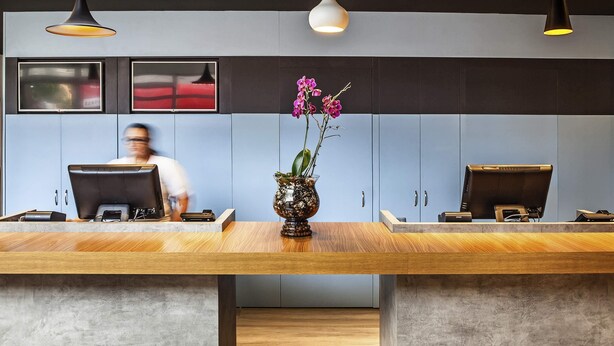 A reception desk with two computer stations, a vase with flowers, and a person in the background.