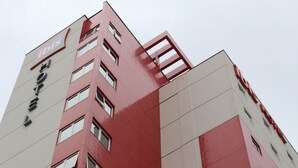 A multi-story hotel building with a red and white facade, multiple windows, and a prominent 'ibis' logo.