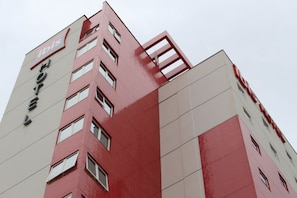 A multi-story hotel building with a red and white facade, multiple windows, and a prominent 'ibis' logo.