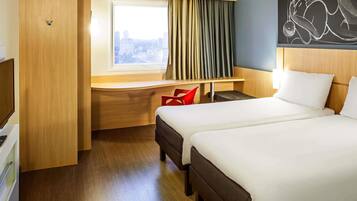A hotel room with two beds, a desk, a red chair, and a city view.
