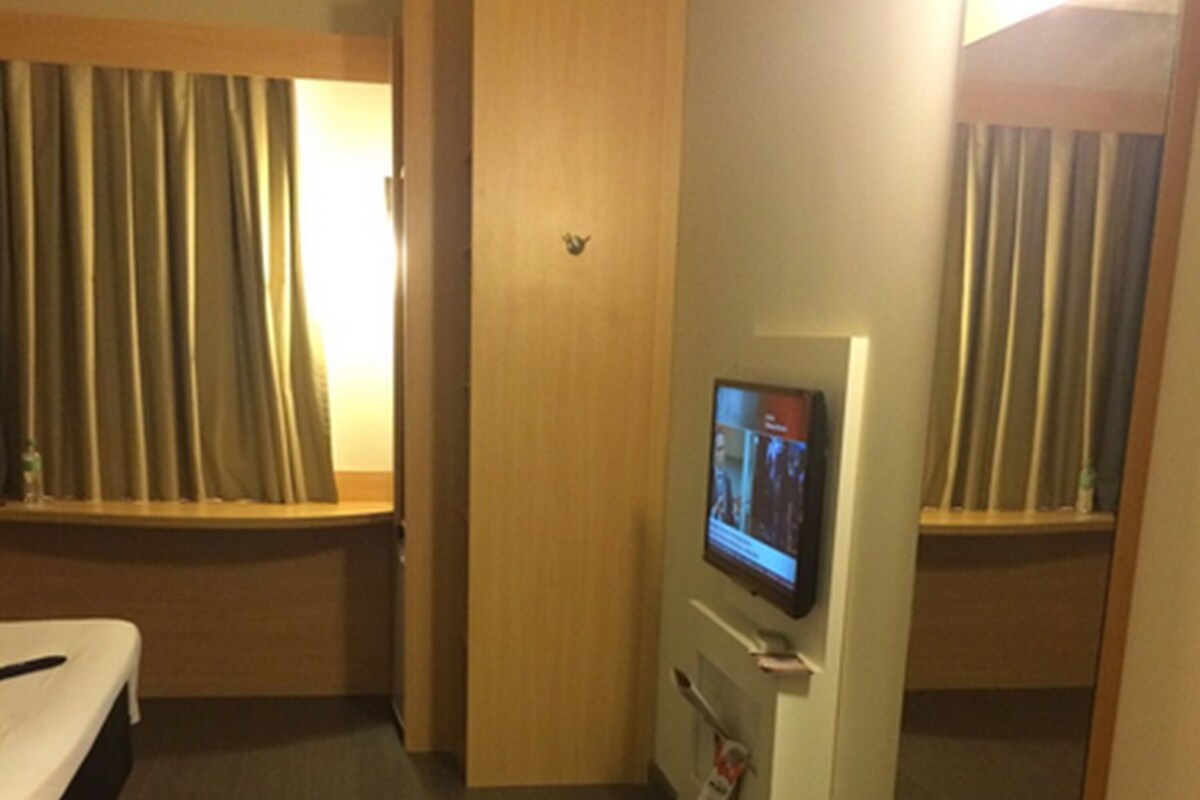 A hotel room with a bed, a television, a red chair, and a window with curtains.