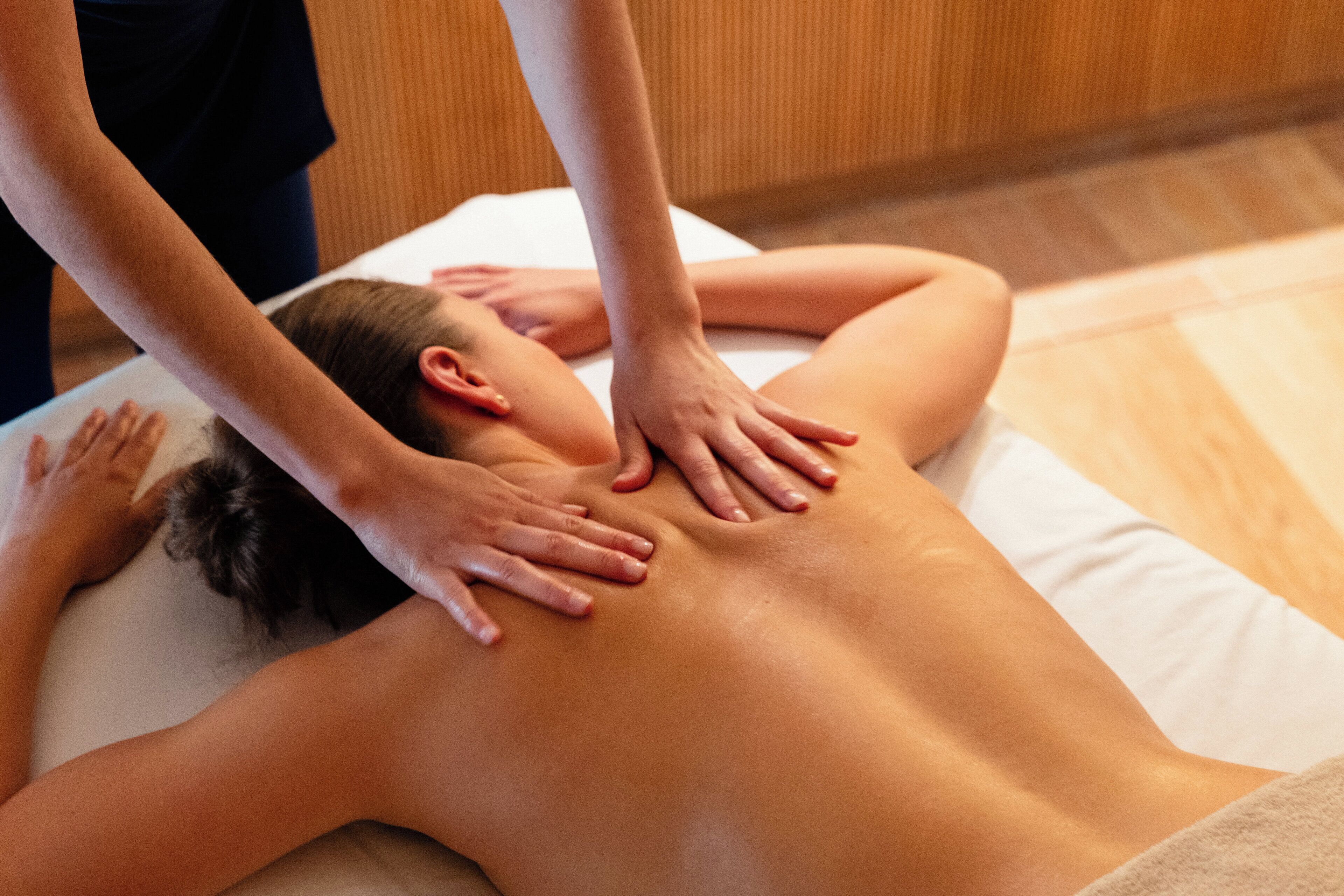 Eine Person erhält eine Rückenmassage auf einer Massageliege in einem Raum mit Holzboden.