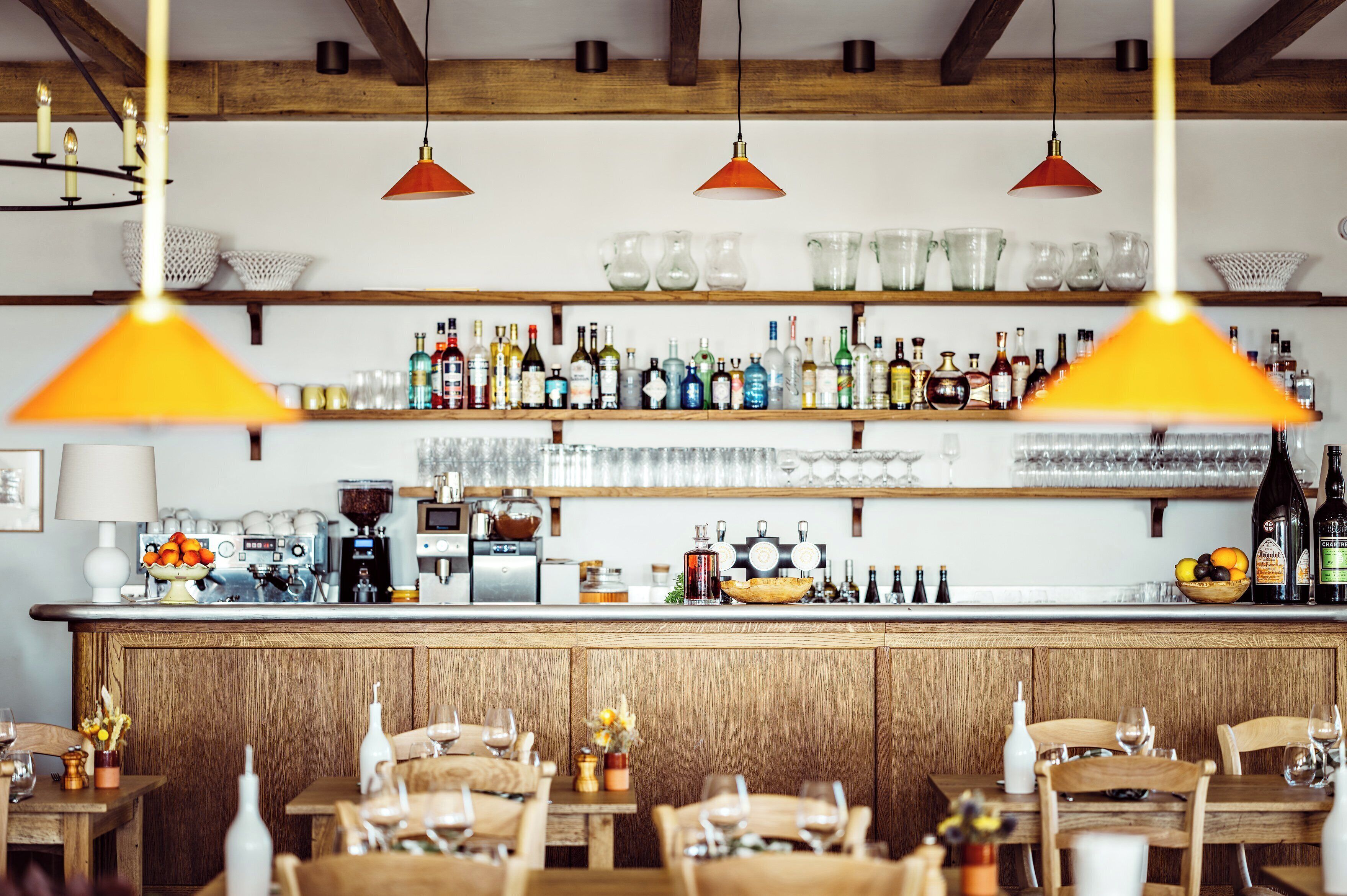 A bar area with a wooden counter, shelves of bottles, and hanging pendant lights.