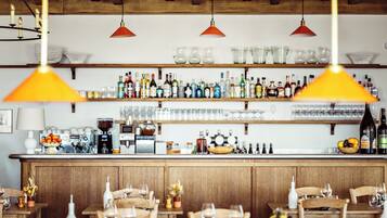 A bar area with a wooden counter, shelves of bottles, and hanging pendant lights.