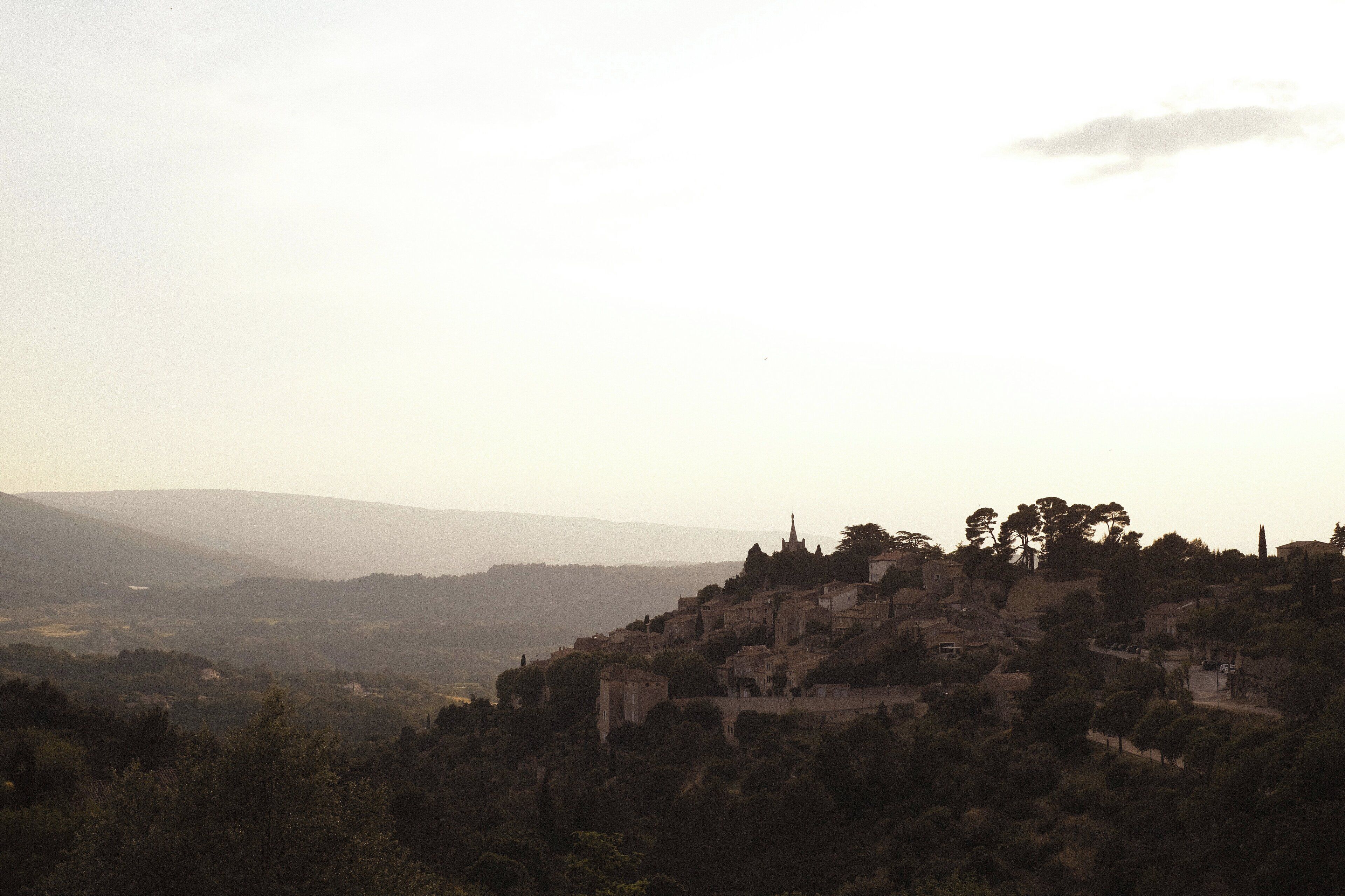 A town with historic buildings on a hill, surrounded by trees and hills in the background.
