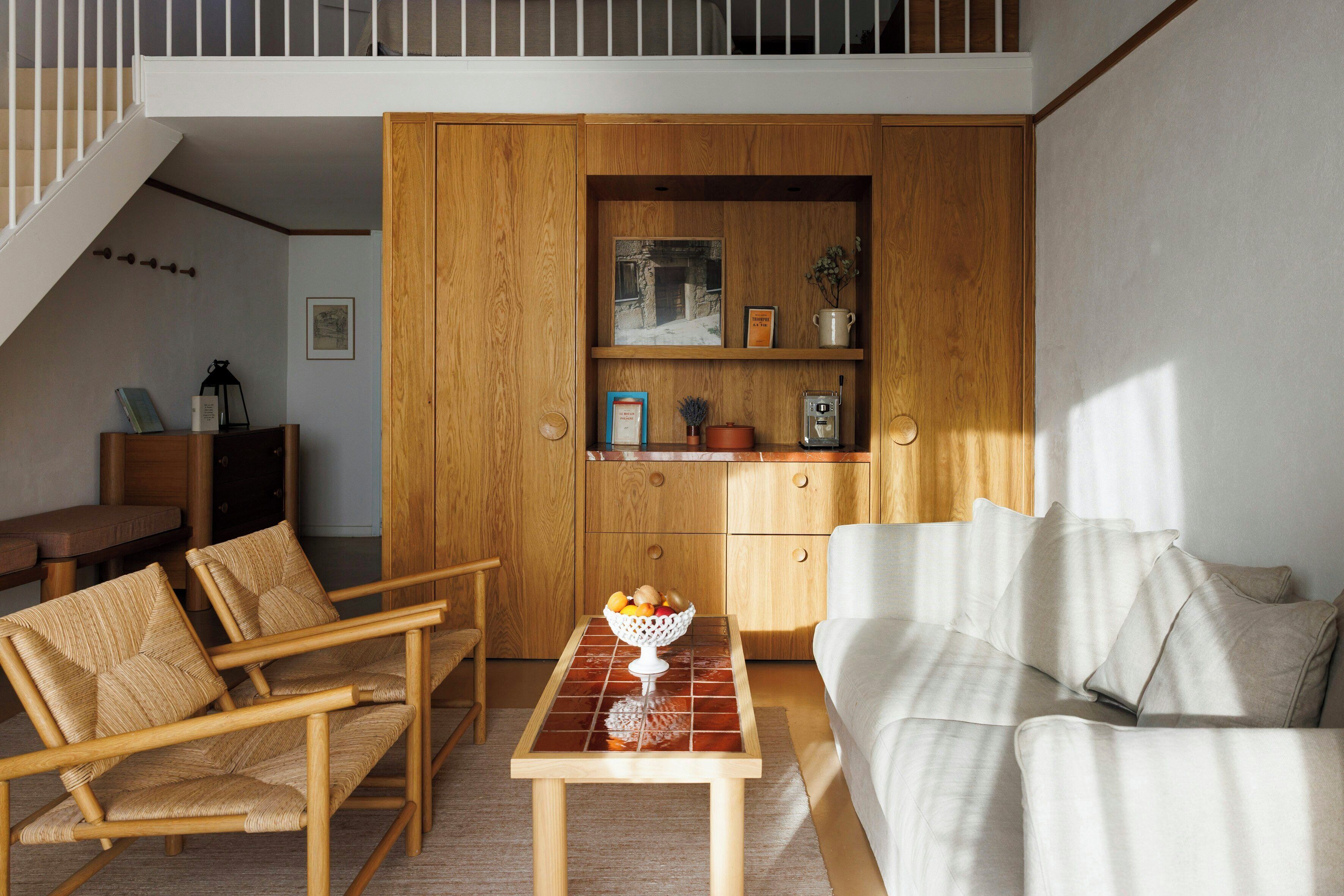 Un espacio habitable pequeño con un sofá, dos sillones, una mesita con un frutero y un mueble de madera con estantes.
