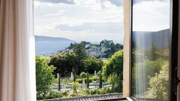 Vista por una ventana que muestra un paisaje con árboles, una piscina y una colina distante.