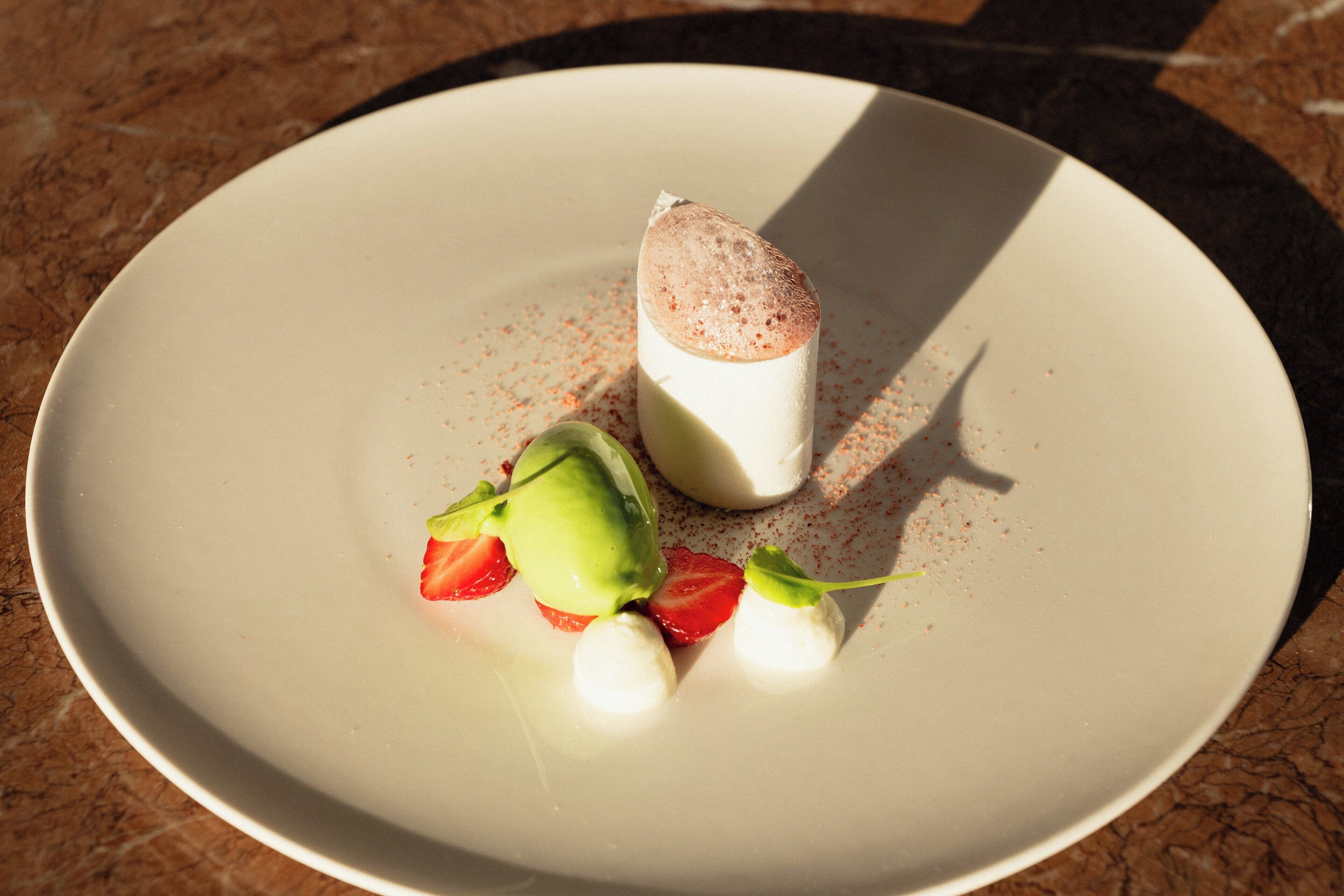 A dessert on a plate with a scoop of ice cream, a scoop of whipped cream, and a strawberry.