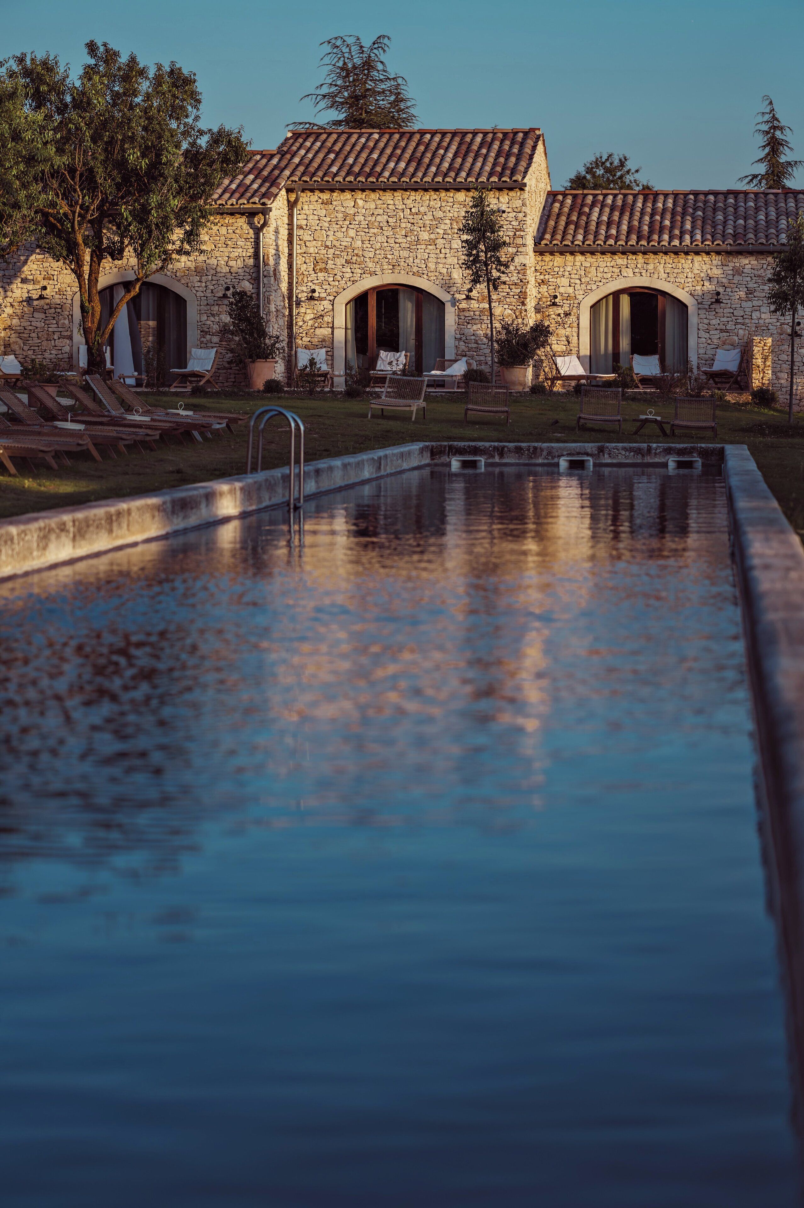 A stone building with a swimming pool, lounge chairs, and a pergola.
