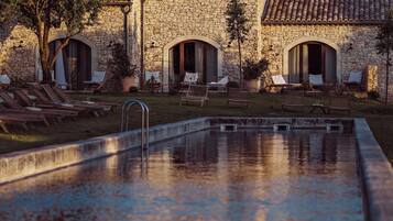 A stone building with a swimming pool, lounge chairs, and a pergola.
