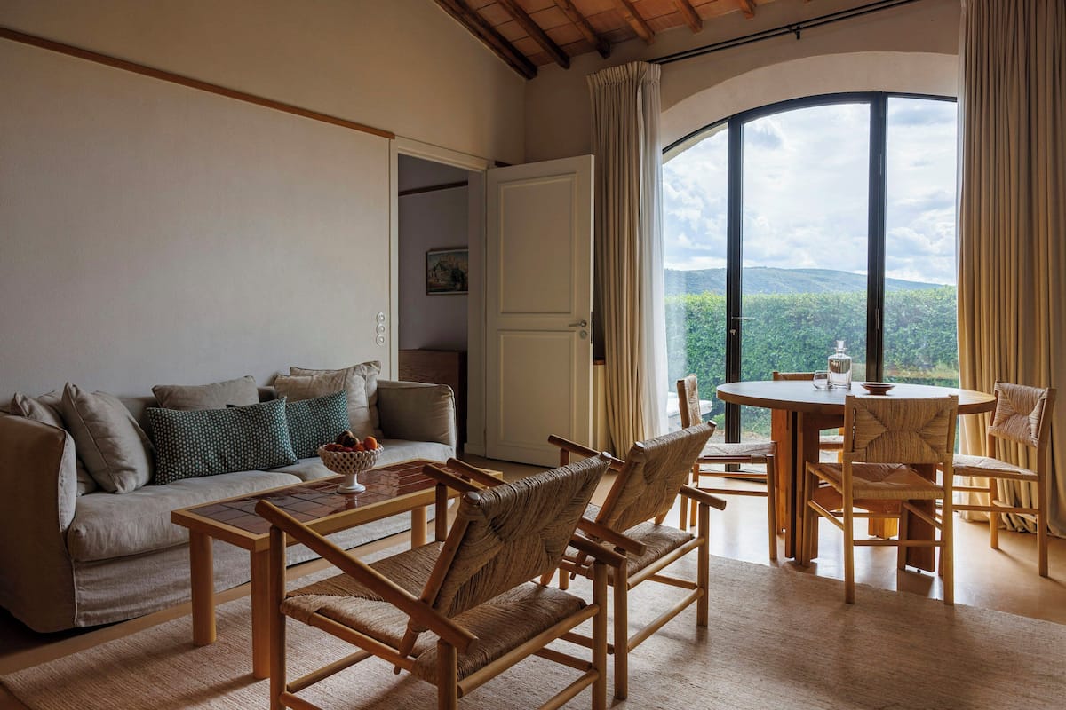 Una sala de estar con sofá, sillas, una mesa y un ventanal con vistas a zonas verdes.