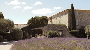 Um edifício de pedra com telhado de telhas, uma ponte de pedra e um campo de lavanda.