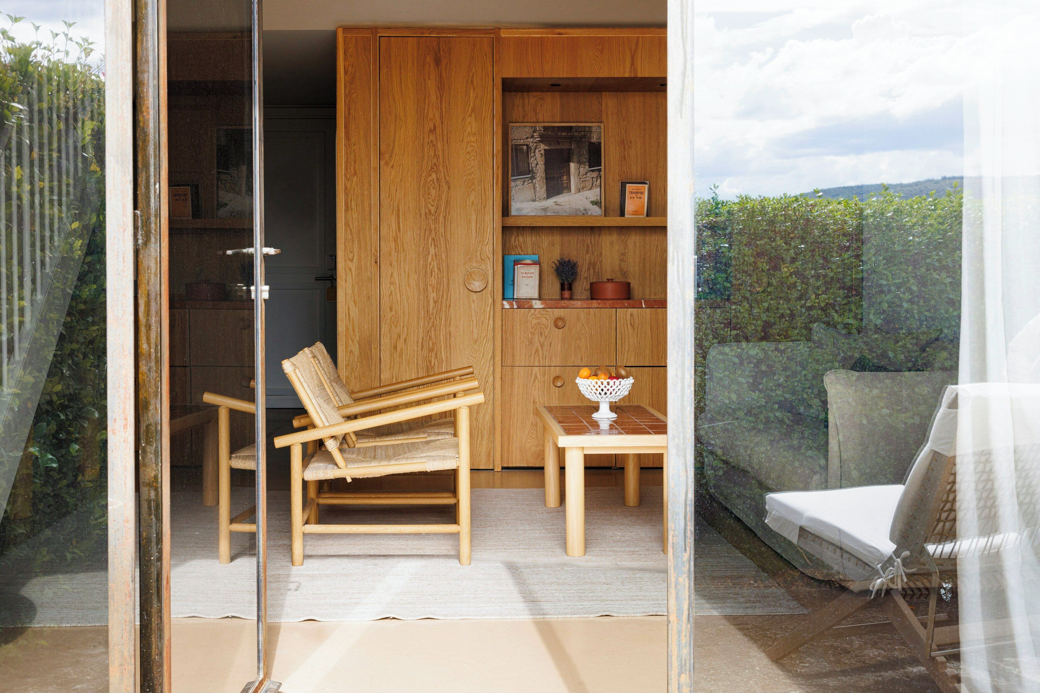 Ein Zimmer mit Holzschrank, Stuhl, Tisch und Blick ins Grüne.