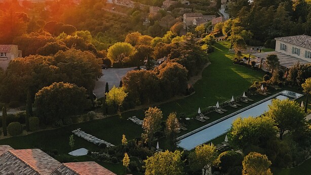 Vista aérea de um bairro residencial com um prédio grande de telhado cerâmico, rodeado por vegetação e piscina.