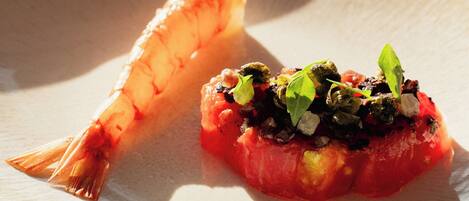 A plate with a shrimp and a tomato-based dish, possibly a tartare, on a textured surface.