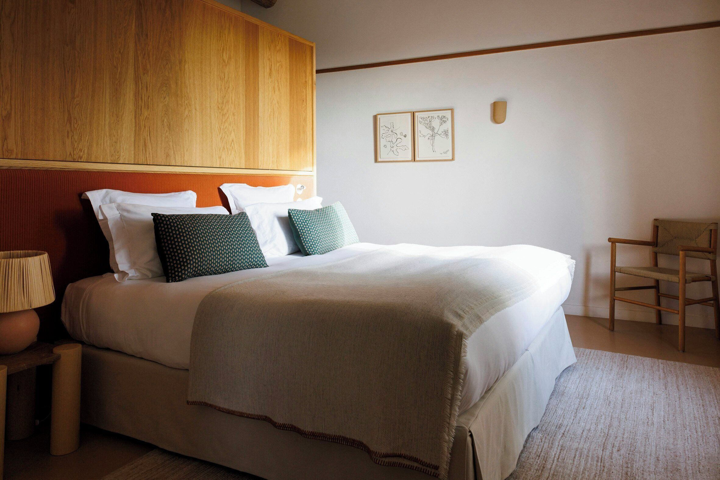 A neatly made bed with pillows, a bedside lamp, and a wooden headboard.