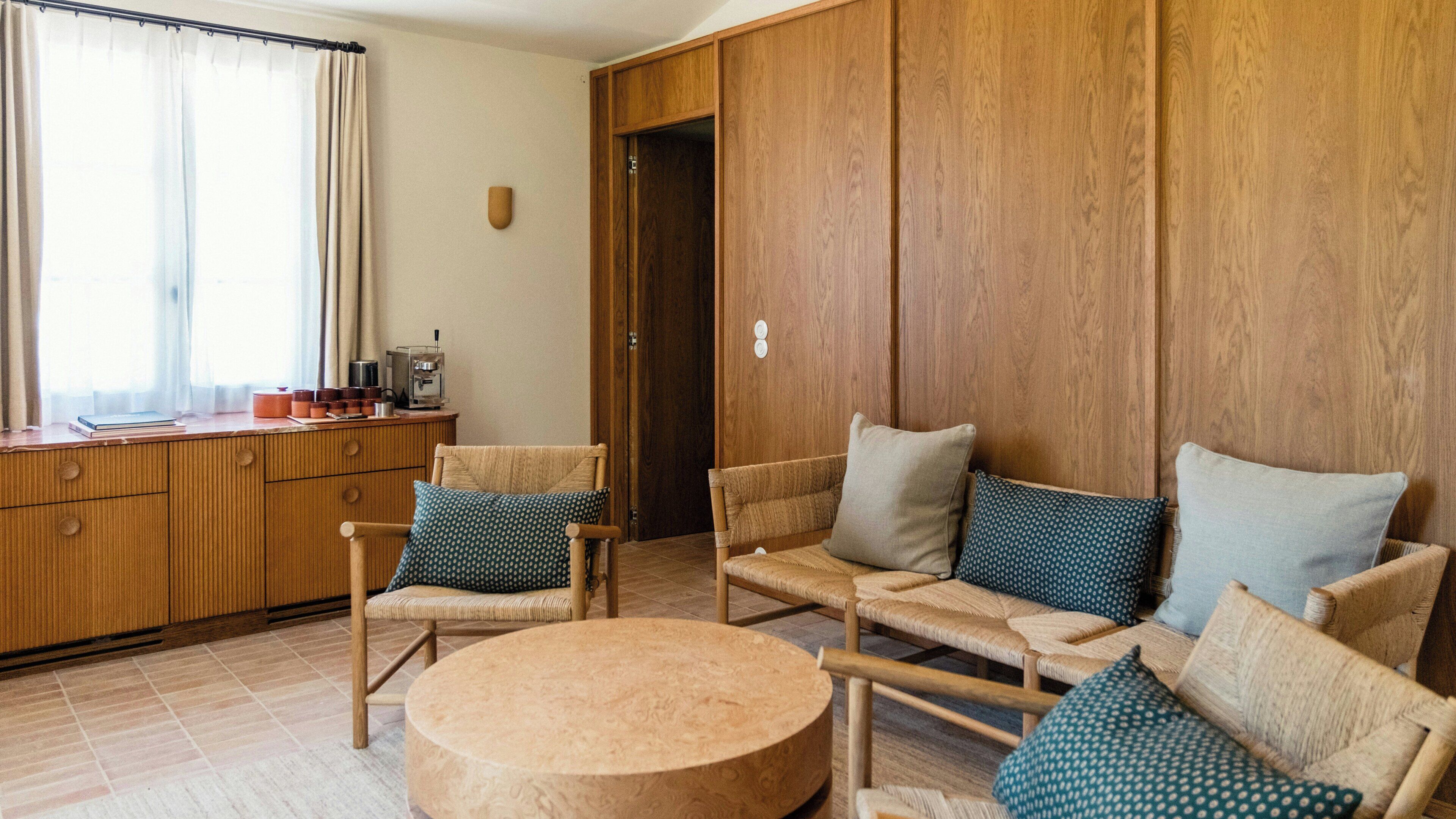 A room with a wooden wardrobe, a coffee machine, and a seating area with chairs and a round table.