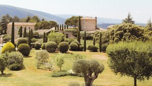 Um jardim ajardinado com sebes bem aparadas, diversas árvores e um pequeno edifício de tijolos.