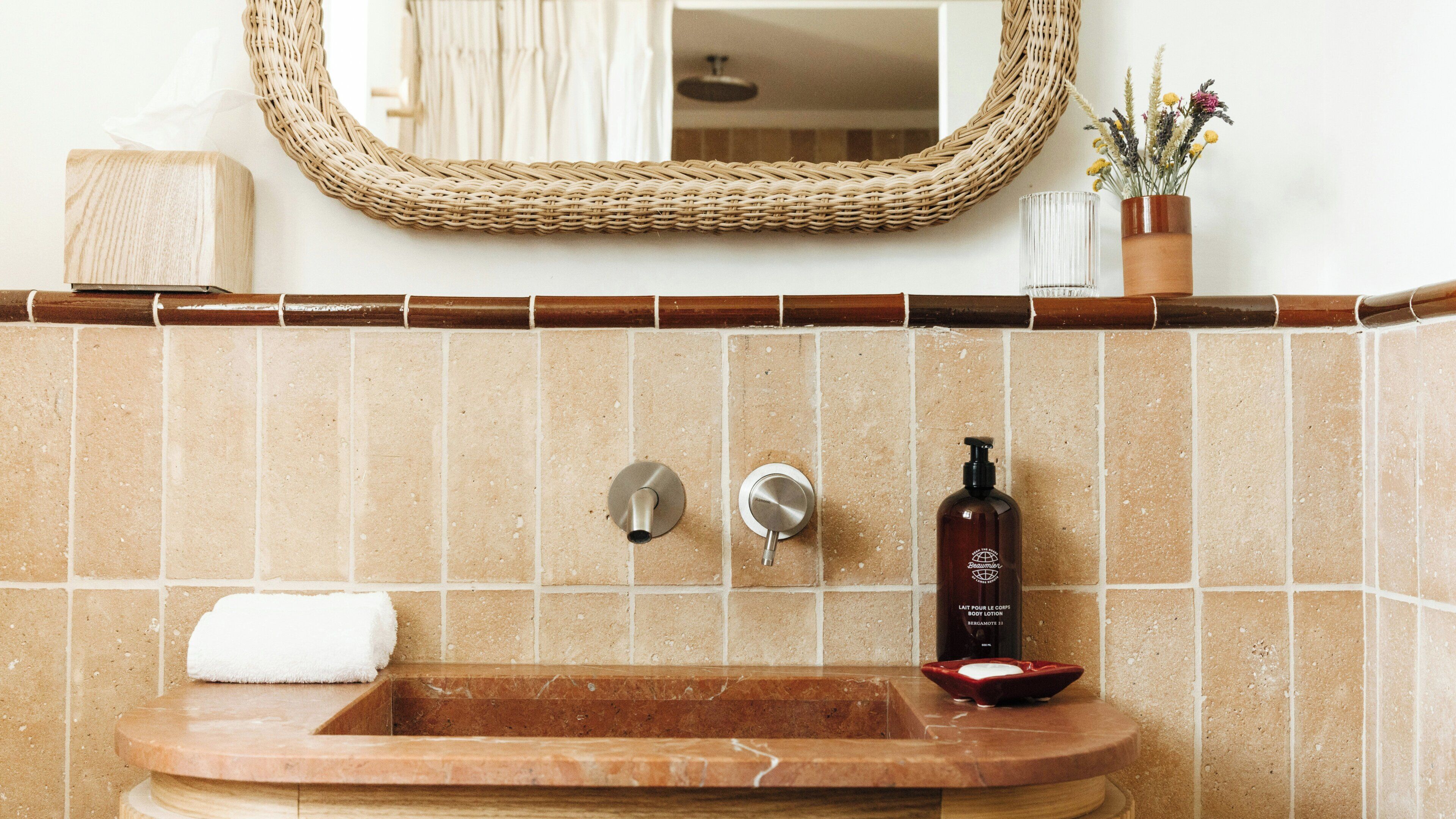 A bathroom with a marble sink, two faucets, a bottle of body lotion, and a towel.