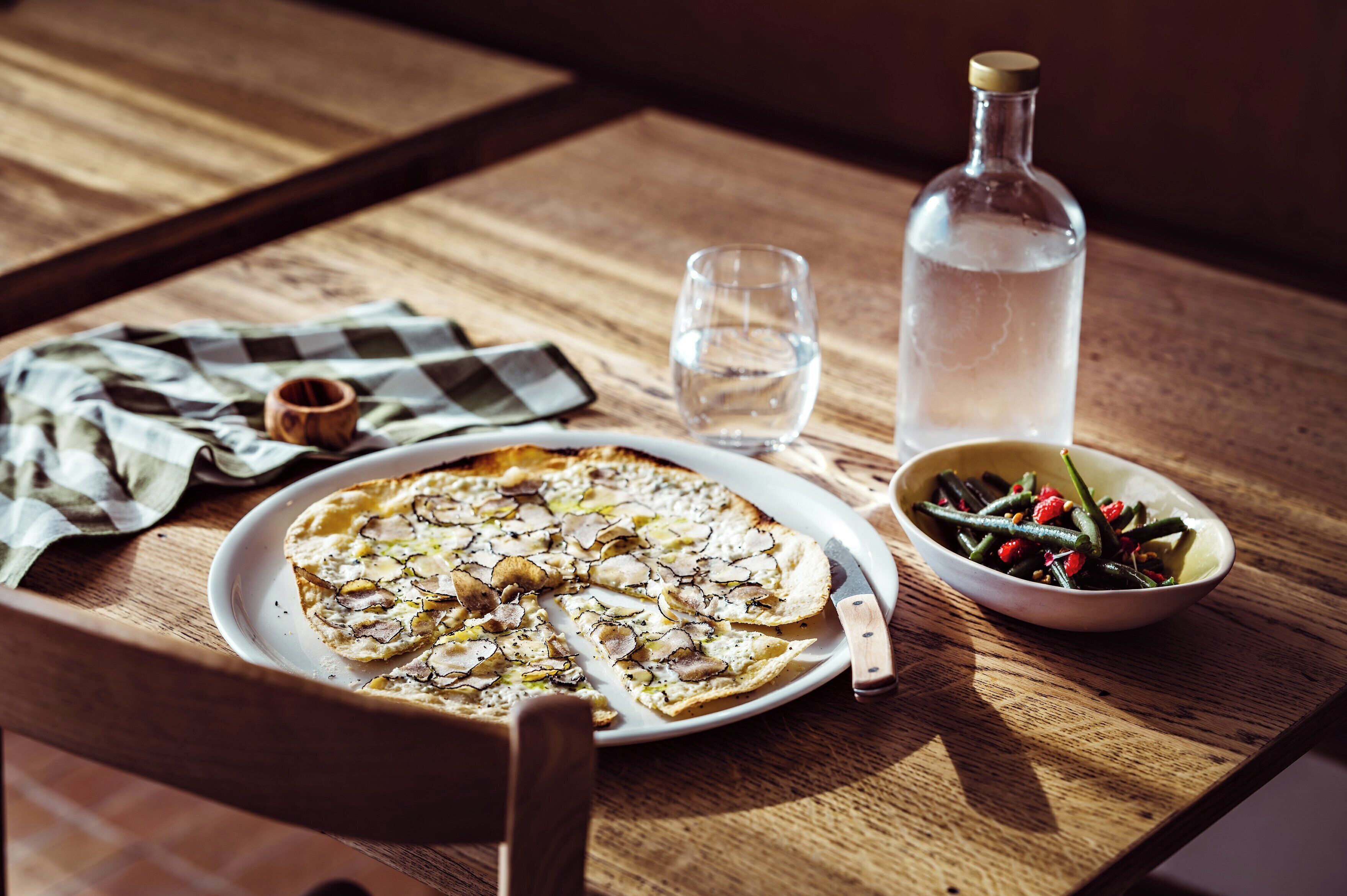 A wooden table with a pizza, a glass of water, a bottle of water, and a bowl of salad.