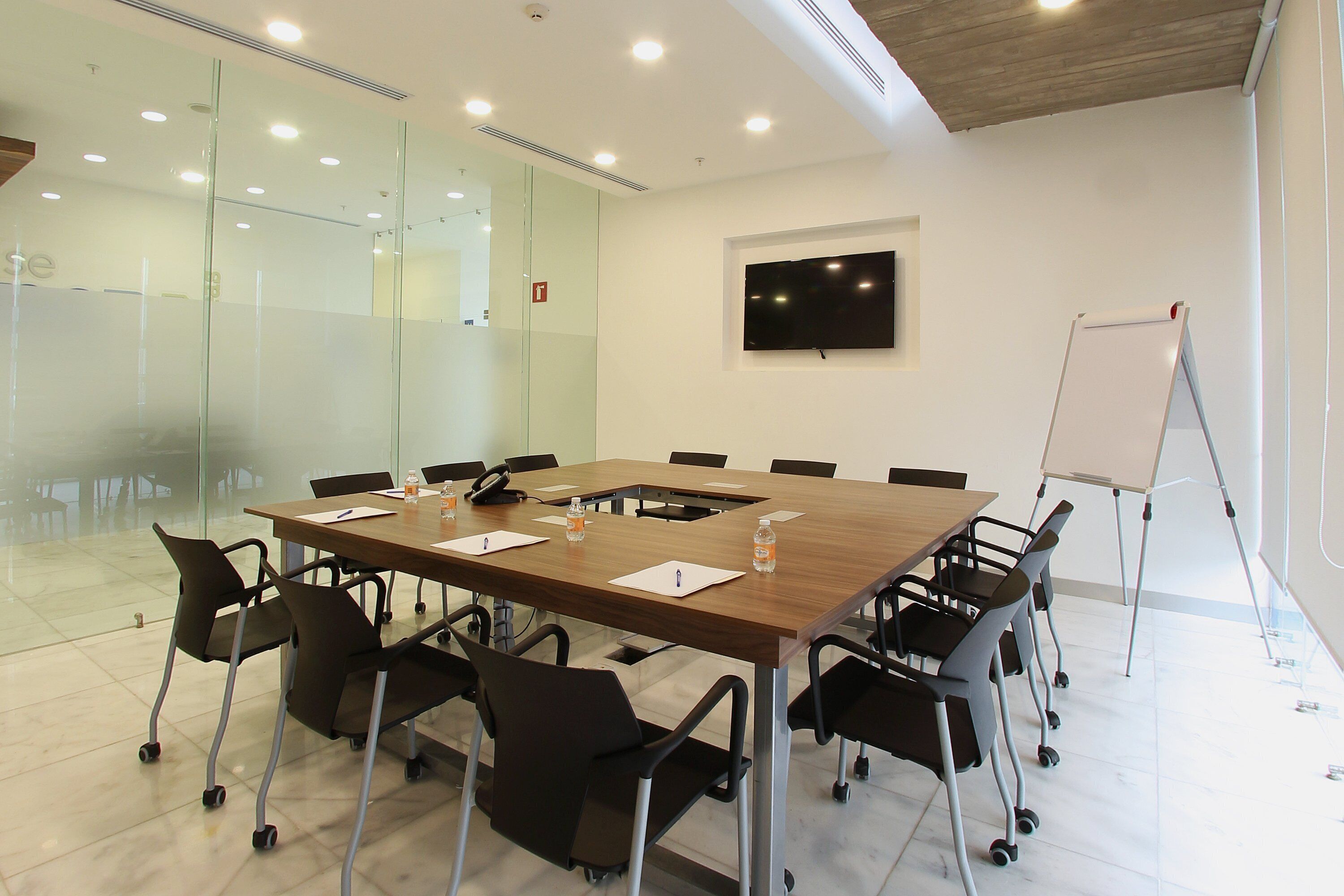 A conference room with a large table, chairs, a whiteboard, and a TV mounted on the wall.