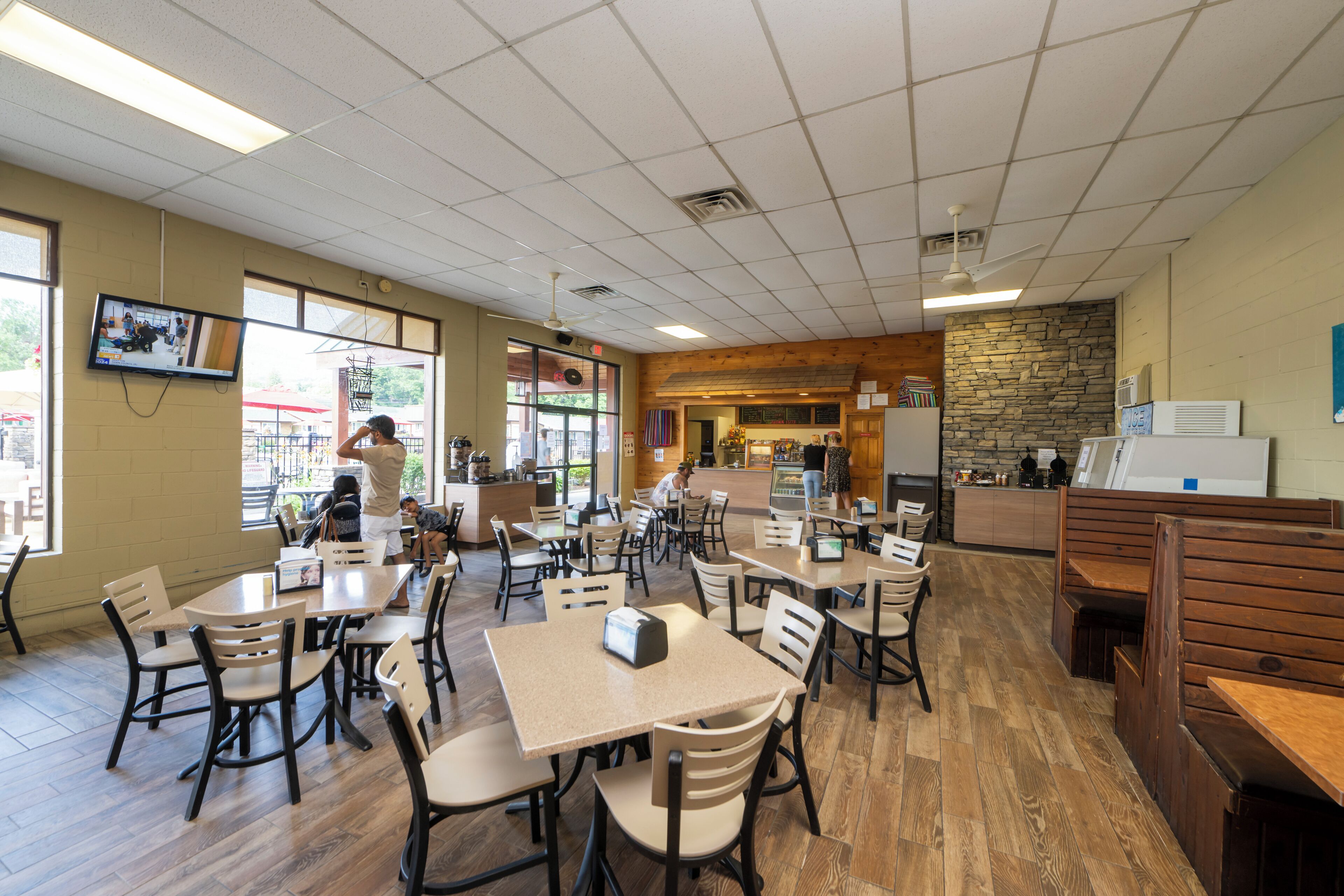 A restaurant with multiple tables and chairs, a counter, and a stone wall.