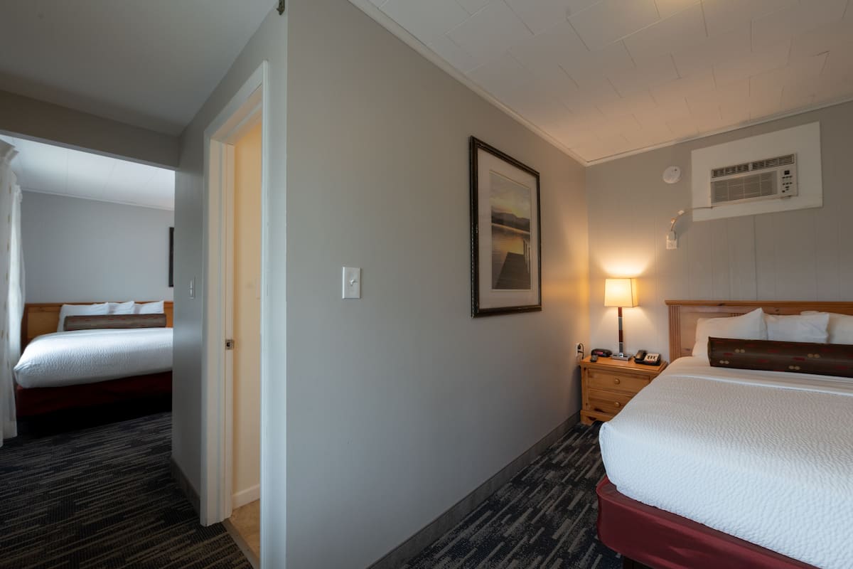 A hotel room with a large bed, a bedside table with a lamp, a framed picture on the wall, and a window with blinds.