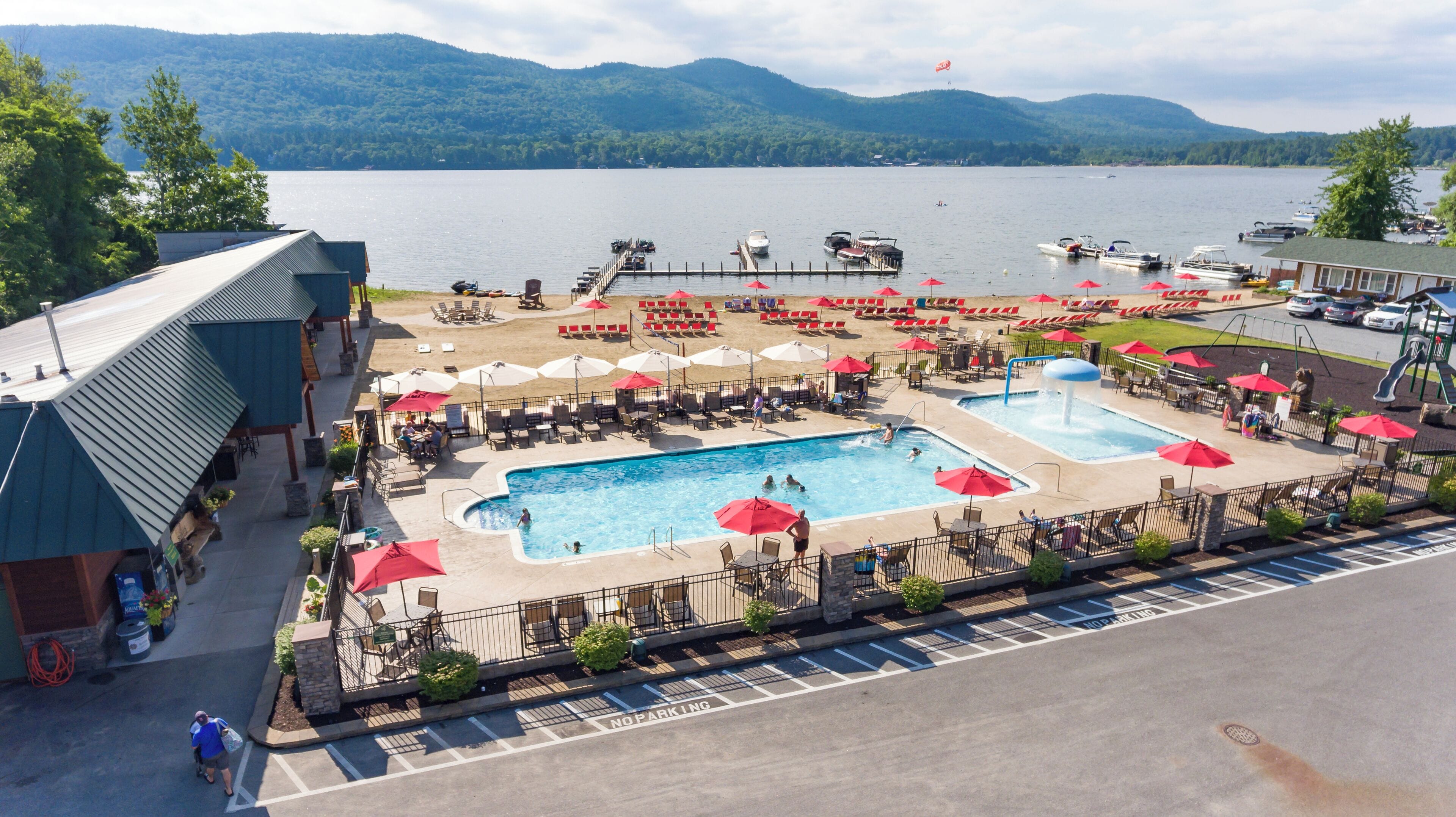 A resort with two swimming pools, lounge chairs, umbrellas, and a view of a lake with boats.
