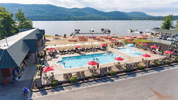 A resort with two swimming pools, lounge chairs, umbrellas, and a view of a lake with boats.