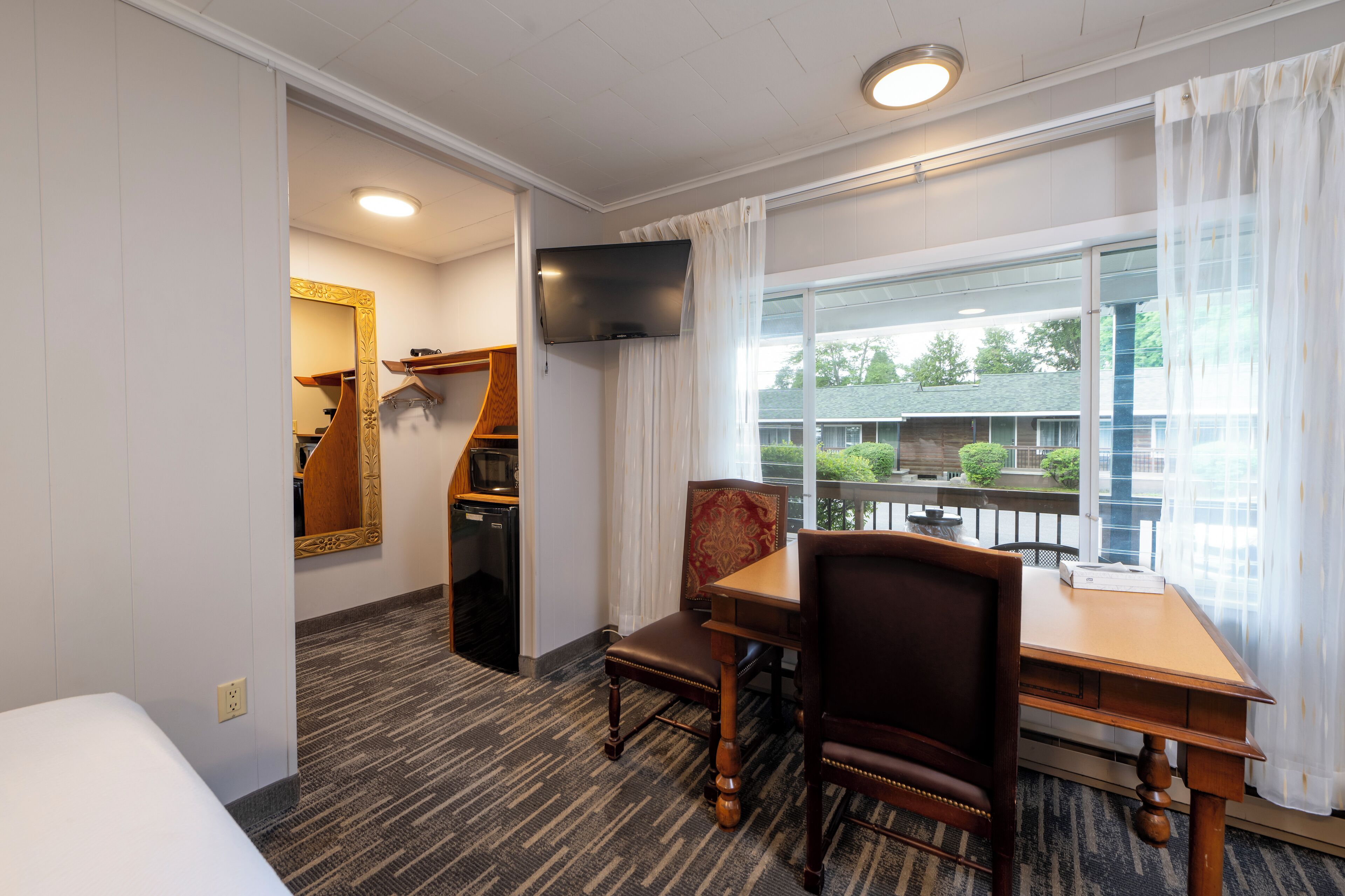 A hotel room with a bed, a dining table with chairs, a TV mounted on the wall, and a window with a view of the outside.
