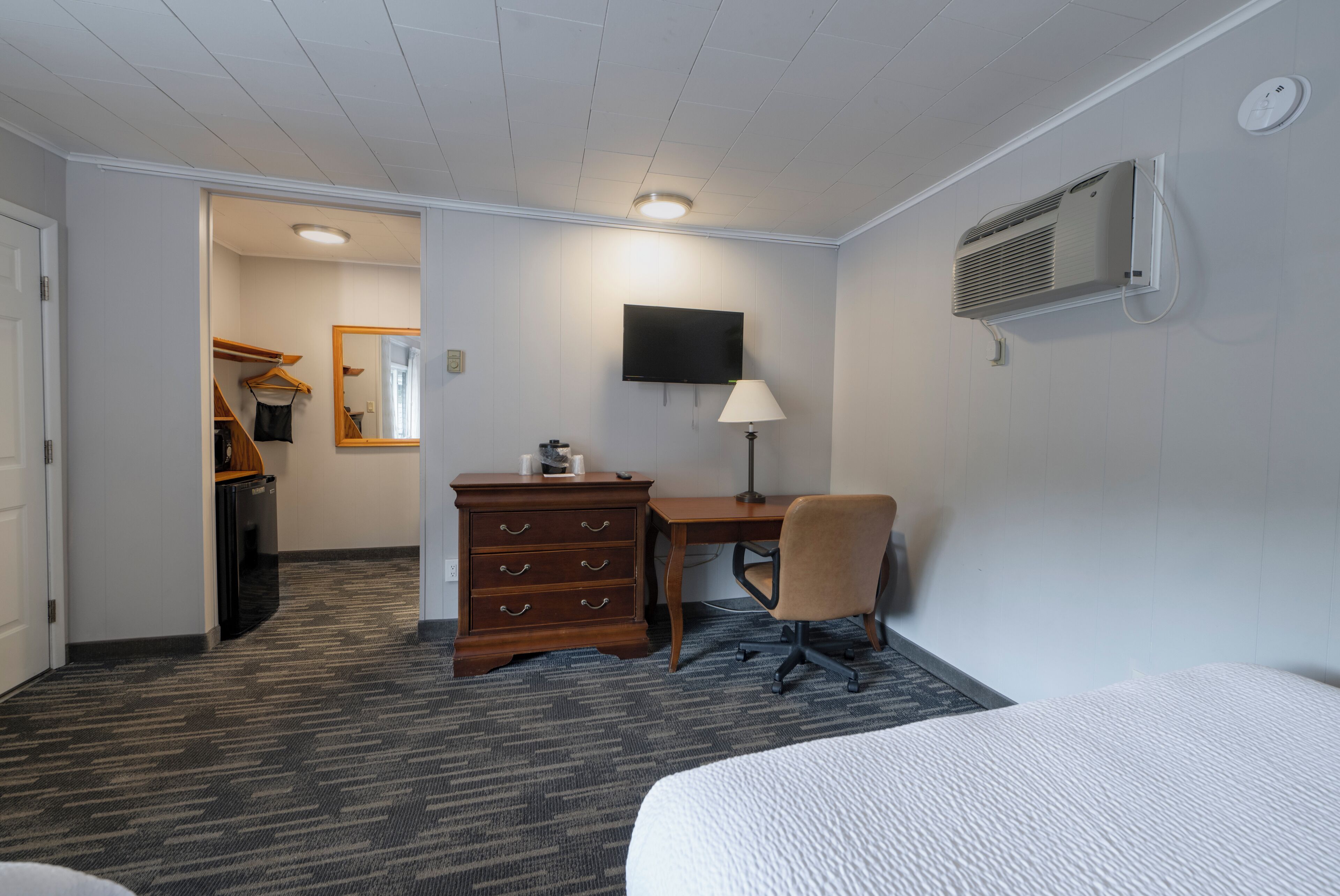 Una habitación de hotel con una cama, un escritorio, una silla, un aparador, un televisor y aire acondicionado instalado en la pared.