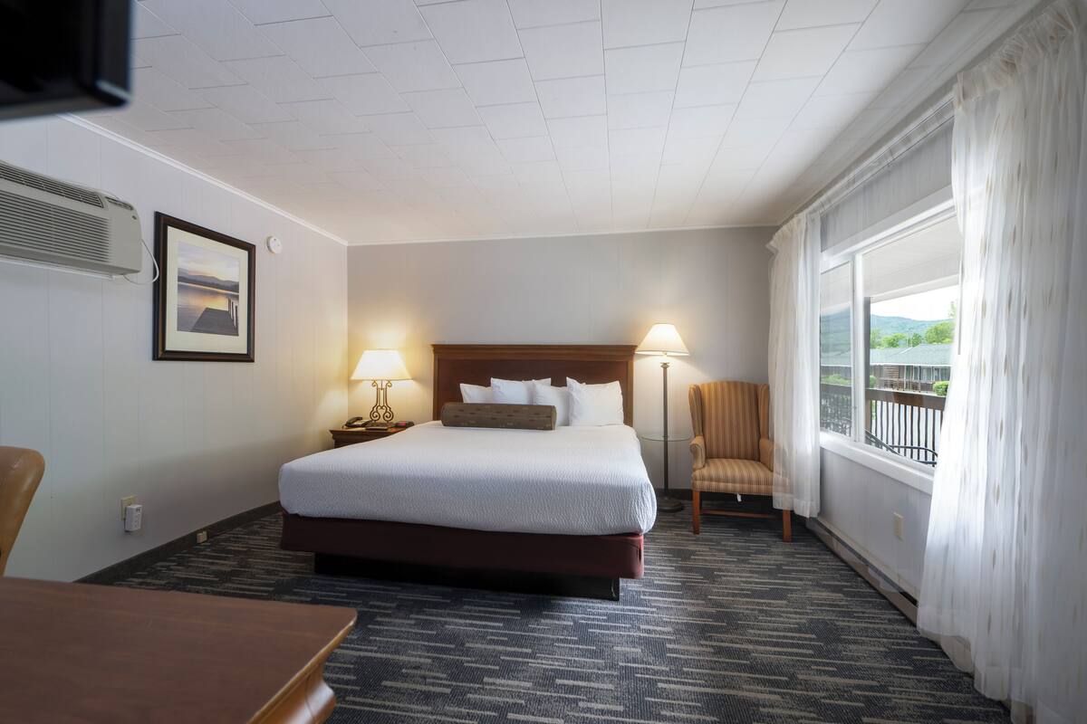 A hotel room with a large bed, two bedside lamps, a chair, a desk, and a window with curtains.