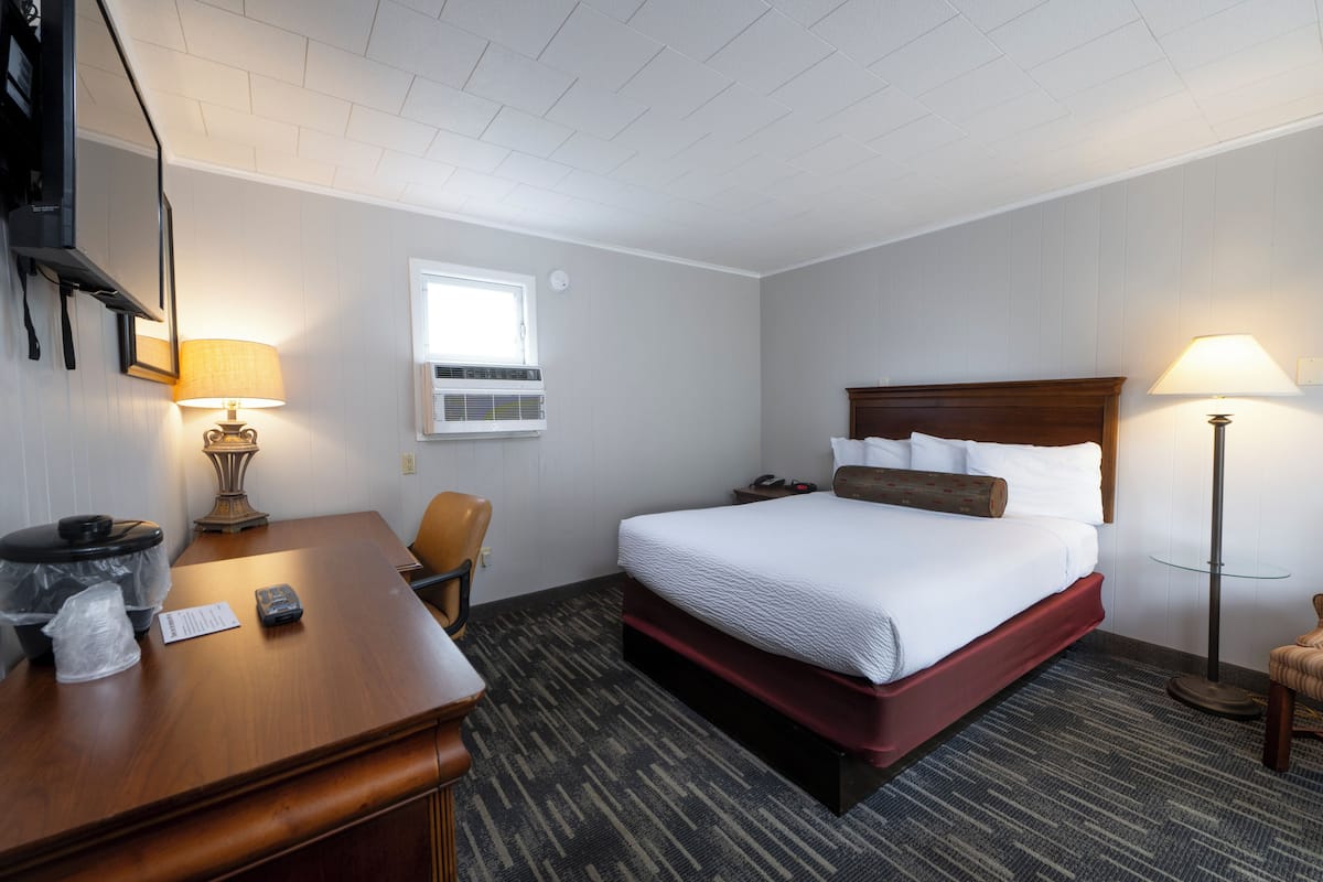 A hotel room with a bed, desk, chair, and two lamps.