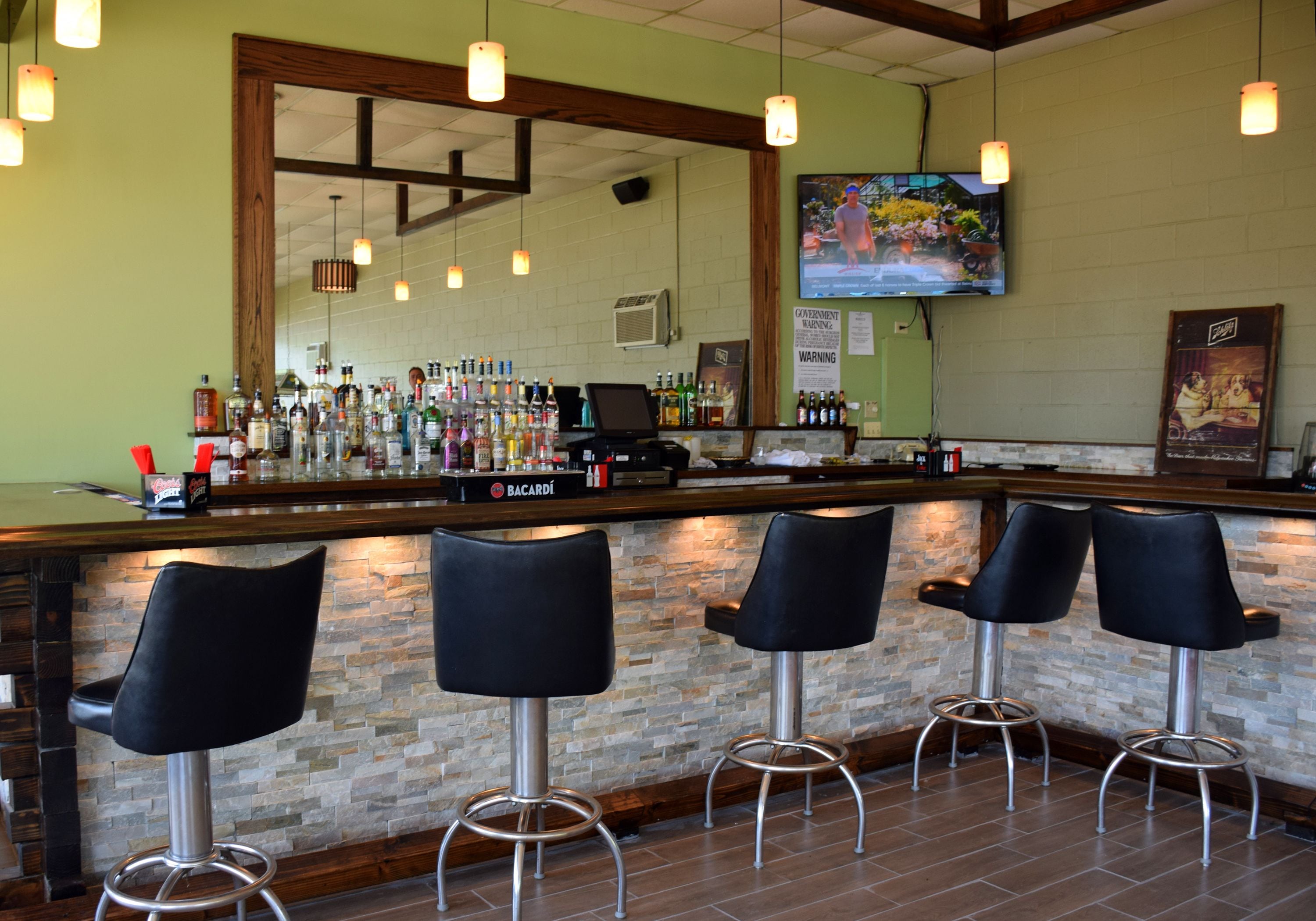 Uma área de bar com parede de pedra, vigas de madeira no teto e banquetas pretas.