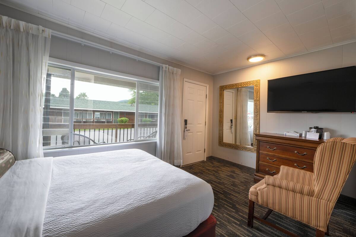 A hotel room with a large bed, a dresser, a television, and a window with curtains.