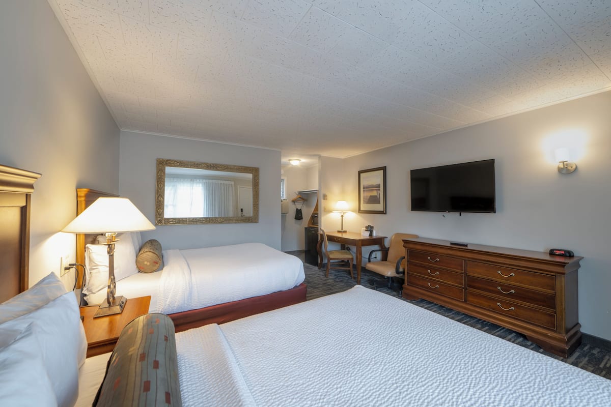 A hotel room with two beds, a desk, a dresser, a TV, and a mirror.